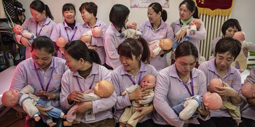BEIJING, CHINA - OCTOBER 28:  Chinese women hold plastic babies as they prepare for a class photo at a course to train to be qualified nannies, known in China as ayis, at the Ayi University on October 28, 2016 in Beijing, China. The Ayi University training program teaches childcare, early education, housekeeping, and other domestic skills. The eight-day course costs US $250, and provides successful participants with a certificate to present to prospective employers. Most of the women attending the program are migrants from villages and cities across China who have moved to the capital to earn income to send home to their own families. China's burgeoning middle class has boosted demand for domestic help in urban areas, and the need for qualified childcare is expected to grow. In 2015, the government dismantled its controversial 'one child policy' as a means of rebalancing China's aging population in order to stave off a demographic crisis. Couples are now allowed to have two children, though the availability and cost of quality childcare is cited as an obstacle for many middle class parents who want larger families.   (Photo by Kevin Frayer/Getty Images)