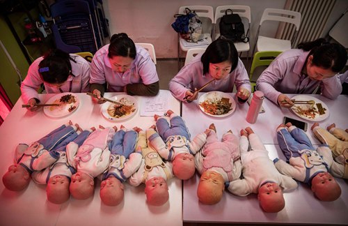 BEIJING, CHINA - OCTOBER 28: Chinese women training to be qualified nannies, known in China as ayis, eat their lunch next to plastic babies used for training during a break in classes at the Ayi University on October 28, 2016 in Beijing, China. The Ayi University training program teaches childcare, early education, housekeeping, and other domestic skills. The eight-day course costs US $250, and provides successful participants with a certificate to present to prospective employers. Most of the women attending the program are migrants from villages and cities across China who have moved to the capital to earn income to send home to their own families. China's burgeoning middle class has boosted demand for domestic help in urban areas, and the need for qualified childcare is expected to grow. In 2015, the government dismantled its controversial 'one child policy' as a means of rebalancing China's aging population in order to stave off a demographic crisis. Couples are now allowed to have two children, though the availability and cost of quality childcare is cited as an obstacle for many middle class parents who want larger families.  (Photo by Kevin Frayer/Getty Images)