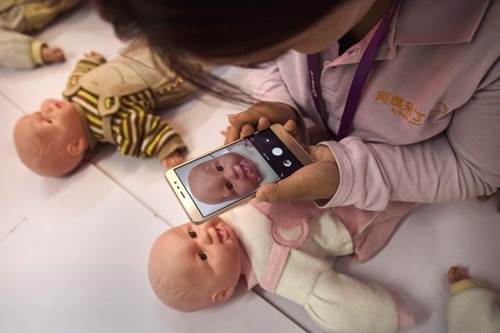 BEIJING, CHINA - OCTOBER 28:  A Chinese woman takes a photo of a plastic baby used in a course as she and others train to be qualified nannies, known in China as ayis, at the Ayi University on October 28, 2016 in Beijing, China. The Ayi University training program teaches childcare, early education, housekeeping, and other domestic skills. The eight-day course costs US $250, and provides successful participants with a certificate to present to prospective employers. Most of the women attending the program are migrants from villages and cities across China who have moved to the capital to earn income to send home to their own families. China's burgeoning middle class has boosted demand for domestic help in urban areas, and the need for qualified childcare is expected to grow. In 2015, the government dismantled its controversial 'one child policy' as a means of rebalancing China's aging population in order to stave off a demographic crisis. Couples are now allowed to have two children, though the availability and cost of quality childcare is cited as an obstacle for many middle class parents who want larger families.   (Photo by Kevin Frayer/Getty Images)